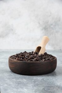 Šviežios kavos pupelės ant medinio šaukšto su aromatinga kava fone